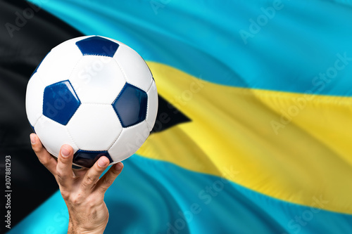 Bahamas soccer concept. National team player hand holding soccer ball with country flag background. Copy space for text.