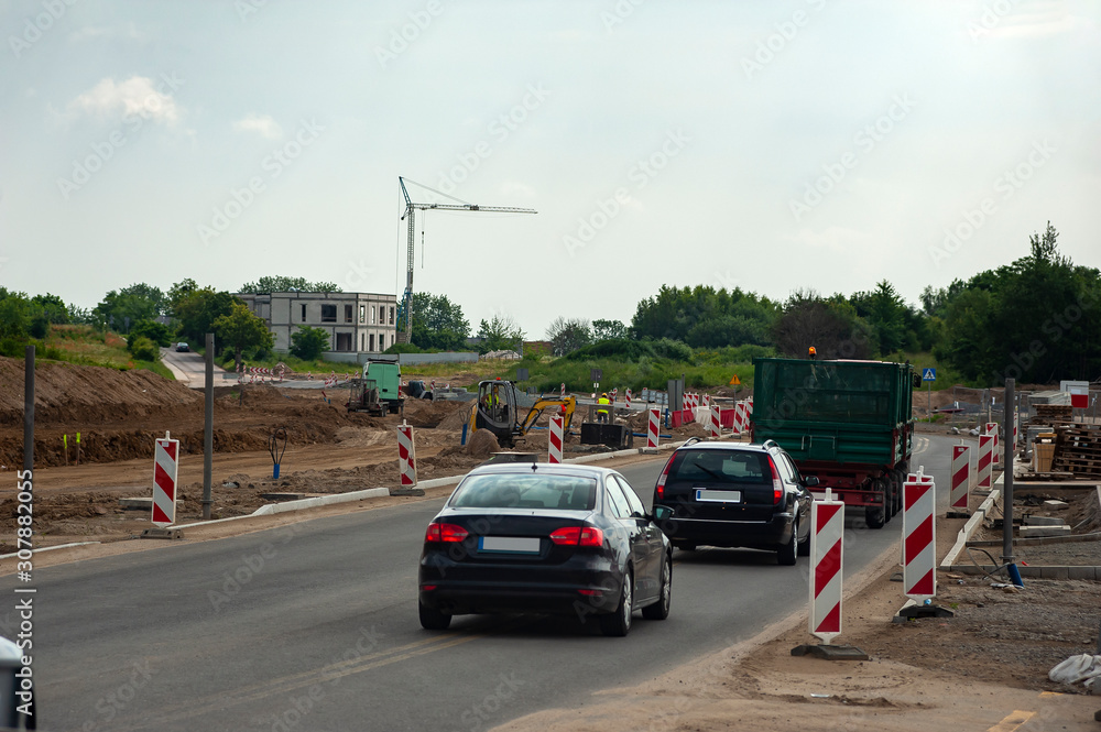 Cars riding on the road works area. Workers are building new road on a summer day.