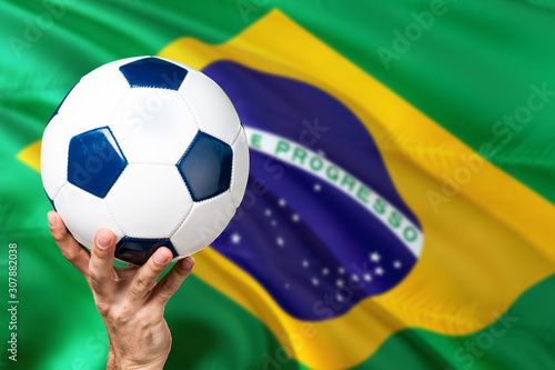 Brazil team soccer concept. National team player hand holding soccer ball with country flag background. Copy space for text.