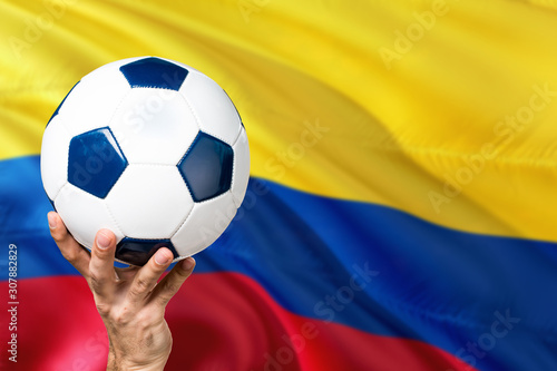 Colombia soccer concept. National team player hand holding soccer ball with country flag background. Copy space for text.