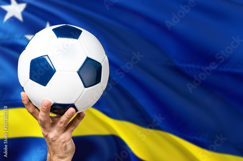 Curacao soccer concept. National team player hand holding soccer ball with country flag background. Copy space for text.