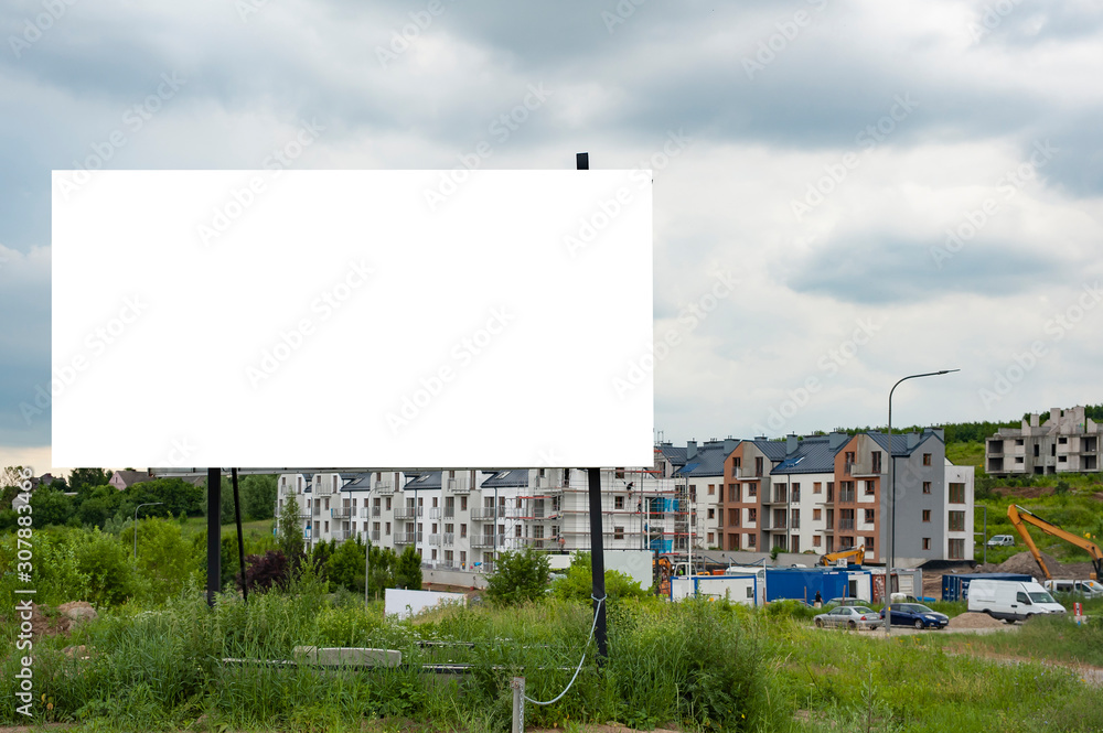 Obraz premium Blank white advertising billboard in the front of construction site on residential area