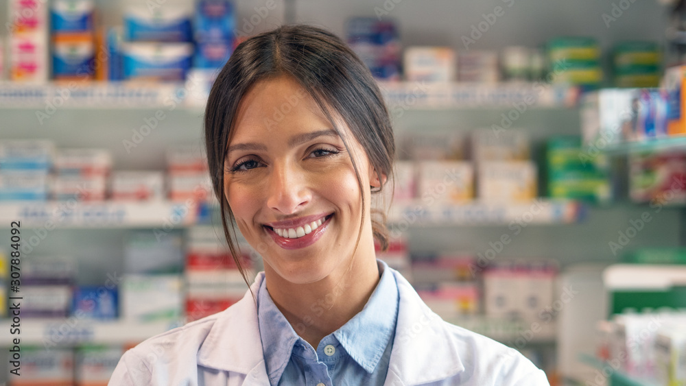 Portrait of an young female pharmacist consultant is smiling in camera in a drug store.