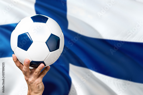 Finland soccer concept. National team player hand holding soccer ball with country flag background. Copy space for text.