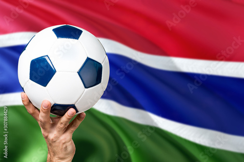 Gambia soccer concept. National team player hand holding soccer ball with country flag background. Copy space for text.
