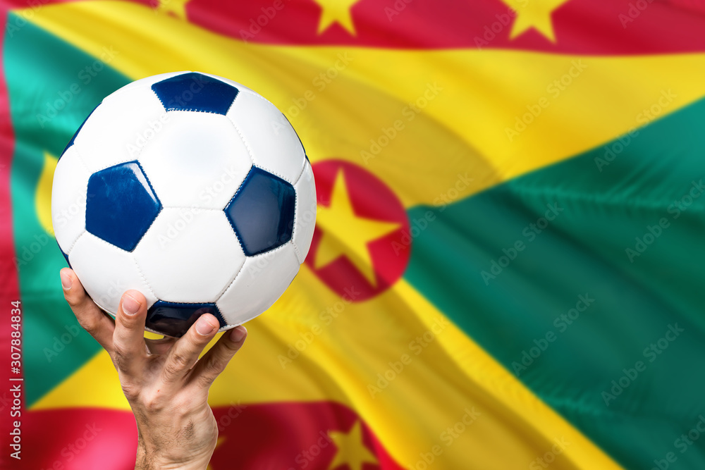 Naklejka premium Grenada soccer concept. National team player hand holding soccer ball with country flag background. Copy space for text.