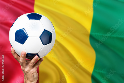 Guinea soccer concept. National team player hand holding soccer ball with country flag background. Copy space for text.
