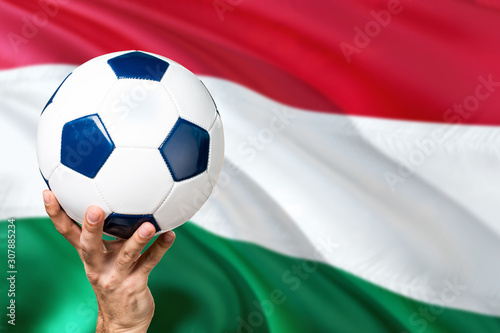 Hungary soccer concept. National team player hand holding soccer ball with country flag background. Copy space for text.