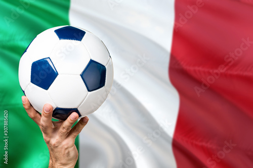 Italy soccer concept. National team player hand holding soccer ball with country flag background. Copy space for text.