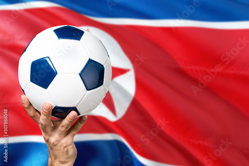 North Korea soccer concept. National team player hand holding soccer ball with country flag background. Copy space for text.