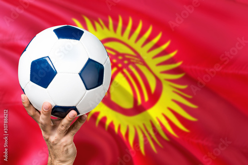 Kyrgyzstan soccer concept. National team player hand holding soccer ball with country flag background. Copy space for text.