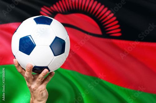 Malawi soccer concept. National team player hand holding soccer ball with country flag background. Copy space for text.