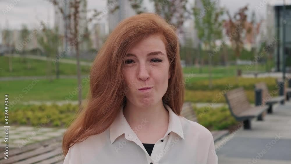 Beautiful young red haired woman in white shirt eating pink doughnut in summer park and smiling. Handheld real time medium shot Beautiful young red haired woman in white shirt eating pink doughnut in summer park and smiling. Handheld real time medium shot