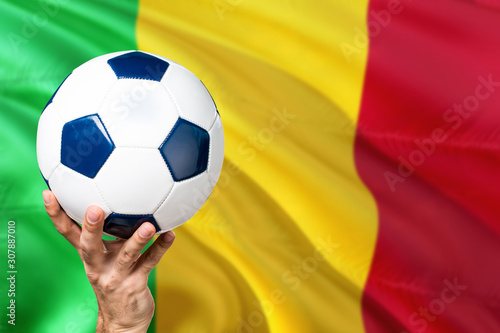 Mali soccer concept. National team player hand holding soccer ball with country flag background. Copy space for text.