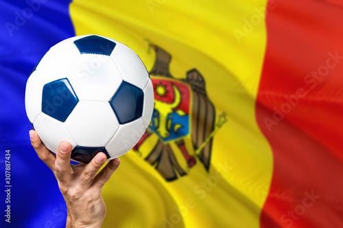 Moldova soccer concept. National team player hand holding soccer ball with country flag background. Copy space for text.
