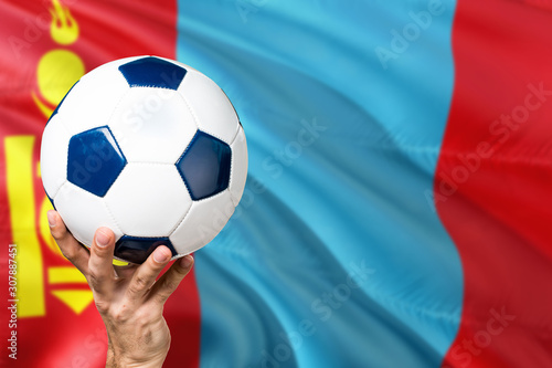 Mongolia soccer concept. National team player hand holding soccer ball with country flag background. Copy space for text.