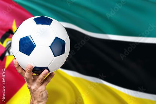 Mozambique soccer concept. National team player hand holding soccer ball with country flag background. Copy space for text.