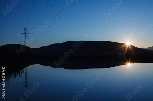 Power line in mountains and sunset reflected in a calm lake