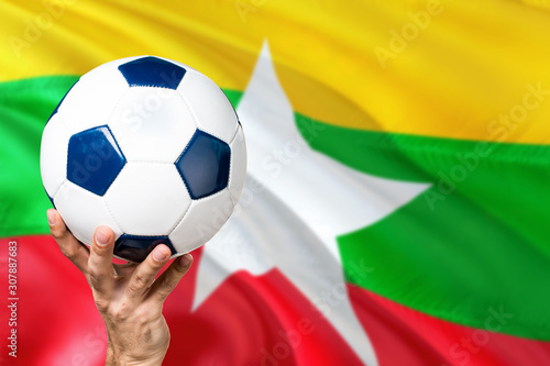 Myanmar soccer concept. National team player hand holding soccer ball with country flag background. Copy space for text.