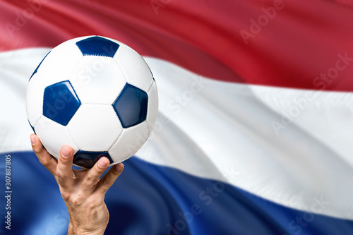 Netherlands soccer concept. National team player hand holding soccer ball with country flag background. Copy space for text.