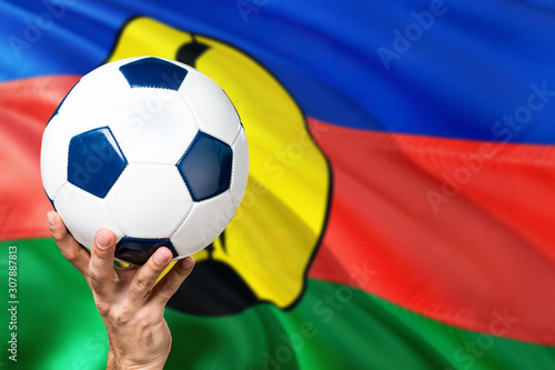 New Caledonia soccer concept. National team player hand holding soccer ball with country flag background. Copy space for text.