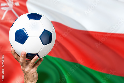 Oman soccer concept. National team player hand holding soccer ball with country flag background. Copy space for text.
