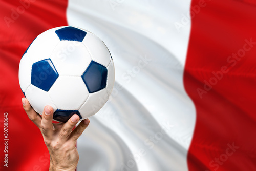 Peru soccer concept. National team player hand holding soccer ball with country flag background. Copy space for text.