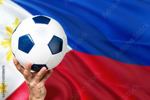 Philippines soccer concept. National team player hand holding soccer ball with country flag background. Copy space for text.