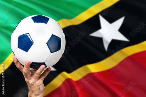 Nevis soccer concept. National team player hand holding soccer ball with country flag background. Copy space for text.