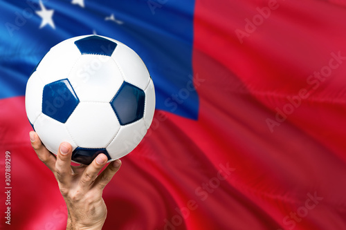 Samoa soccer concept. National team player hand holding soccer ball with country flag background. Copy space for text.