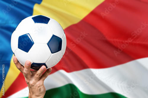 Seychelles soccer concept. National team player hand holding soccer ball with country flag background. Copy space for text.