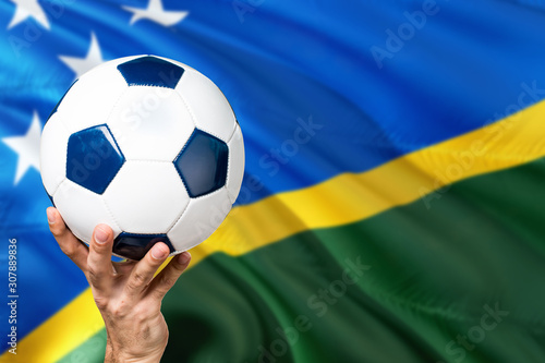 Solomon Islands soccer concept. National team player hand holding soccer ball with country flag background. Copy space for text.