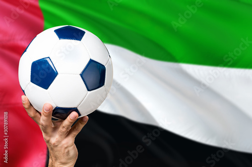 United Arab Emirates soccer concept. National team player hand holding soccer ball with country flag background. Copy space for text.