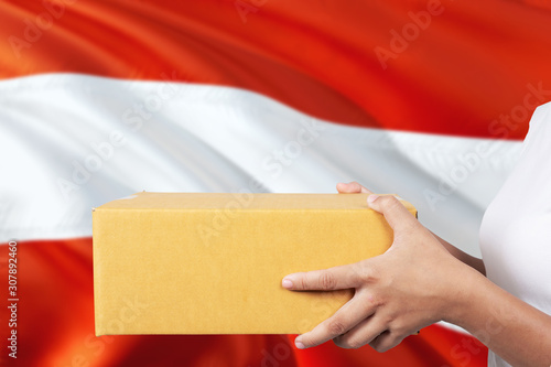 Austria delivery service. International shipment theme. Woman courier hand holding brown box isolated on national flag background.