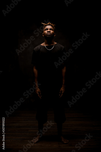 Black man with blonde dreadlocks posing in the dark outfit looking up