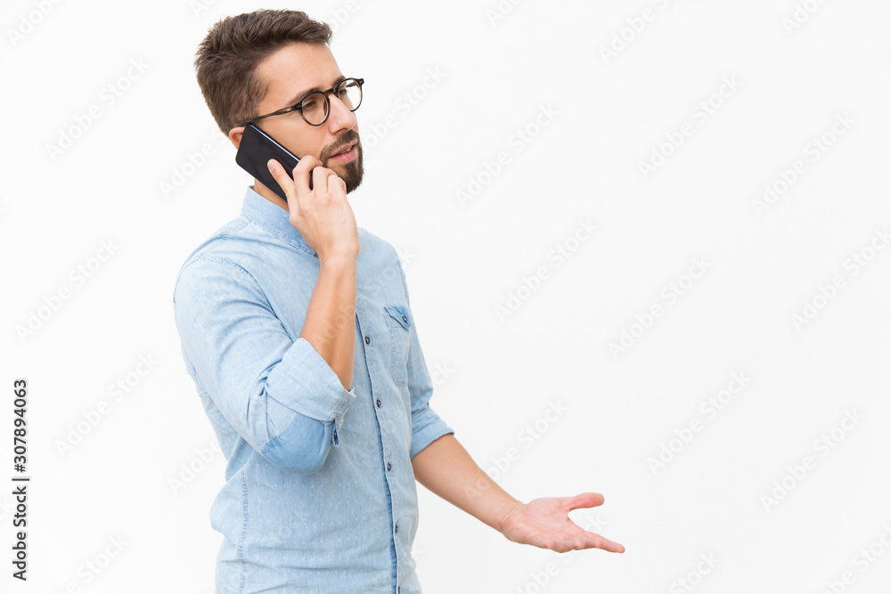 Annoyed guy speaking on mobile phone, arguing with talk partner. Handsome young man in casual shirt and glasses standing isolated over white background. Phone talk concept Annoyed guy speaking on mobile phone, arguing with talk partner. Handsome young man in casual shirt and glasses standing isolated over white background. Phone talk concept