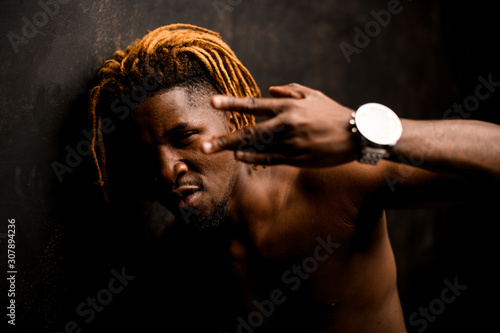 Naked black guy with blonde dreadlocks posing in the studio looking at camera showing finger gest