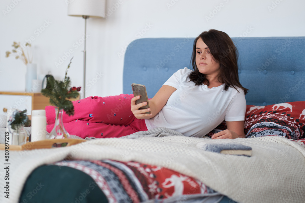 middle-aged woman resting at home. lady relaxed on bed uses her phone, social network concept