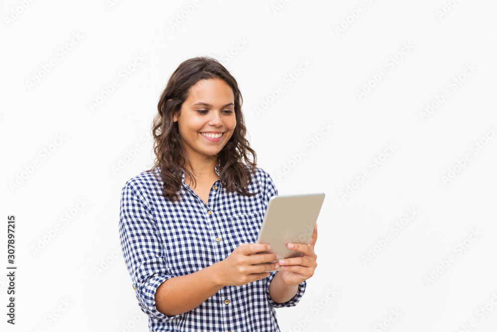 Happy cheerful student girl using tablet, reading content on screen. Young woman in casual checked shirt standing isolated over white background. Wireless communication concept Happy cheerful student girl using tablet, reading content on screen. Young woman in casual checked shirt standing isolated over white background. Wireless communication concept
