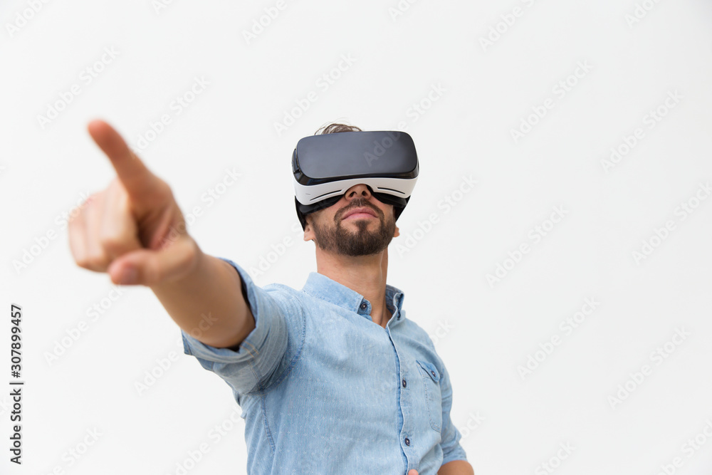 Handsome bearded guy wearing VR glasses, touching air with finger. Young man in virtual reality headset standing isolated over white background. VR presentation concept Handsome bearded guy wearing VR glasses, touching air with finger. Young man in virtual reality headset standing isolated over white background. VR presentation concept
