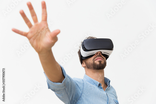 Bearded guy in VR glasses using virtual simulator. Young man in virtual reality headset standing isolated over white background. VR simulation concept