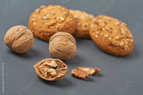 Walnuts beside homemade cookies with seeds of sunflower and sesame lies on dark scratched concrete table on kitchen. Close-up