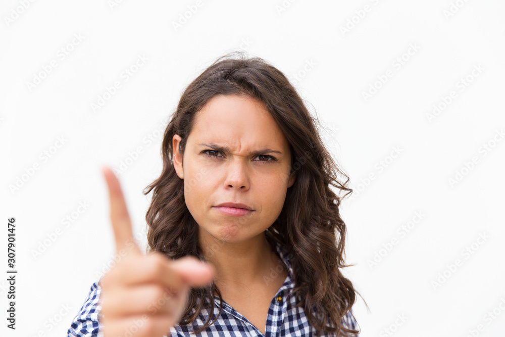 Strict frowning Latin woman shaking finger at camera. Young woman in casual checked shirt standing isolated over white background. Threaten gesture concept Strict frowning Latin woman shaking finger at camera. Young woman in casual checked shirt standing isolated over white background. Threaten gesture concept