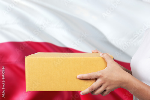 Poland delivery service. International shipment theme. Woman courier hand holding brown box isolated on national flag background.