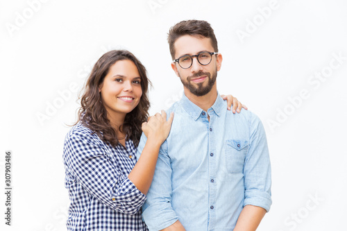 Positive Latin woman hugging male friend, couple smiling at camera. Young woman in casual and man in glasses standing isolated over white background. Couple or friendship concept