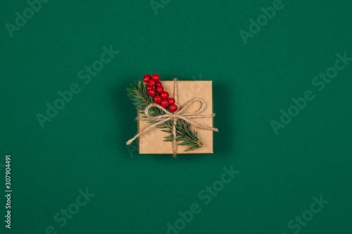 Craft gift box with spruce branch and red berries on green background. Holiday eco-friendly concept.