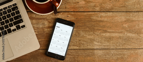 Screen of smartphone with calendar of year 2020 with laptop, pen and organizer on coffee table photo