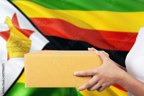 Zimbabwe delivery service. International shipment theme. Woman courier hand holding brown box isolated on national flag background.