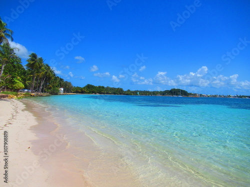 Une plage de sable blanc et la mer turquoise sous un ciel bleu sans nuage