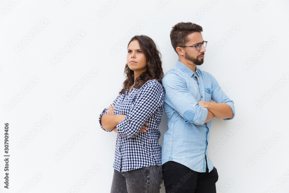 Annoyed upset couple standing back-to-back with arms crossed. Young woman in casual and man in glasses posing isolated over white background. Conflict in couple concept Annoyed upset couple standing back-to-back with arms crossed. Young woman in casual and man in glasses posing isolated over white background. Conflict in couple concept